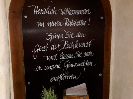 Speisetafel mit dem Text Herzlich willkommen im neuen Ratskeller! Spüren Sie den Geist der Kochkunst und lassen Sie sich in unsere Genusswelten entführen!