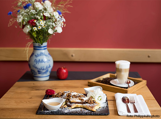 Anschaulich gedeckter Tisch mit einem Blumenstrauß, einem Apfel, Dessert und Kaffee darauf